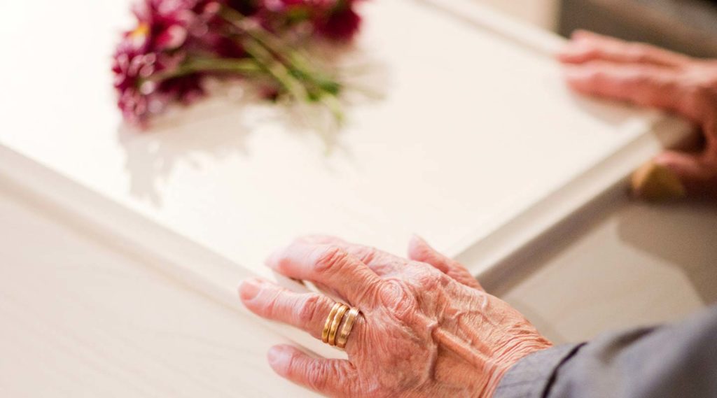 Begravning. Närbild på en äldre persons händer på en ljus kista. Foto Alex & Martin IKON.