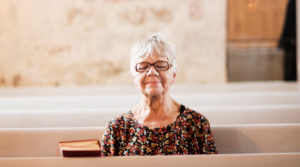 Kvinna med slutna ögon som sitter i en kyrka. Foto Alex o Martin.